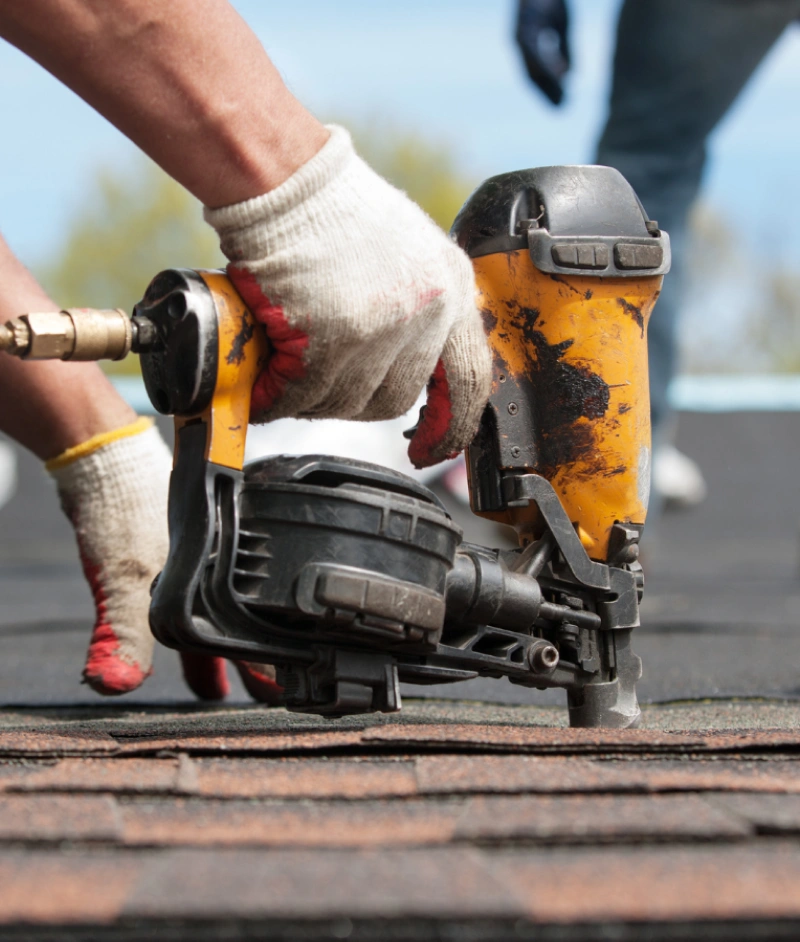 Roofer working with nail gun on roofing project